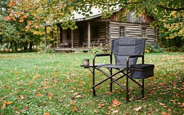 A director’s camp chair with a side table, on a cottage lawn under maple trees