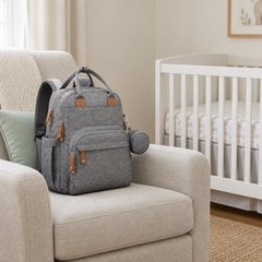 RUVALINO diaper bag backpack, sitting on a nursery armchair beside a white crib