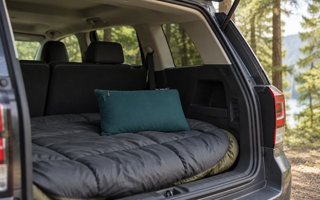 Memory foam camping pillow, on a sleeping bag in the back of an SUV set up for car camping, the hatch open to the trees