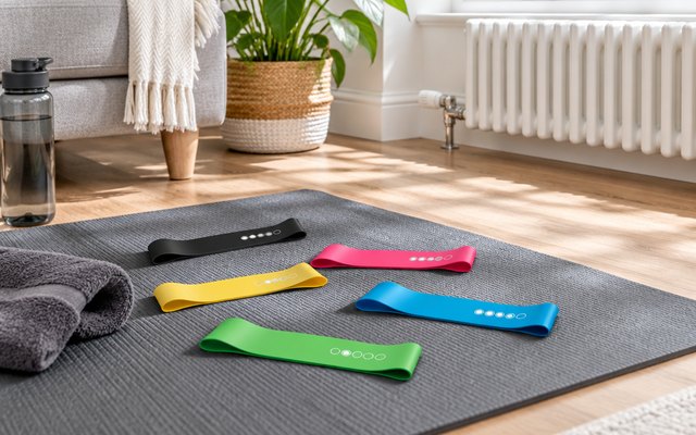 Gritin mini loop bands, lying loosely on a yoga mat on the floor of a bright living room beside a radiator
