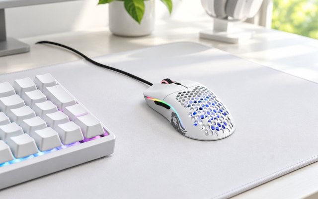 Glorious Model O, on a white desk mat beside a keyboard in a bright gaming setup