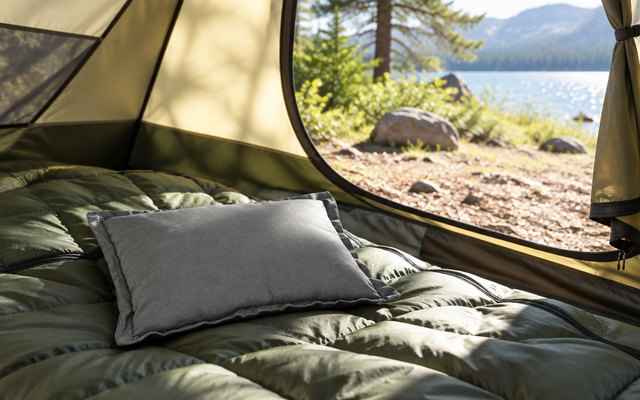Grey travel pillow on a sleeping bag inside a tent, the door open to a sunny campsite