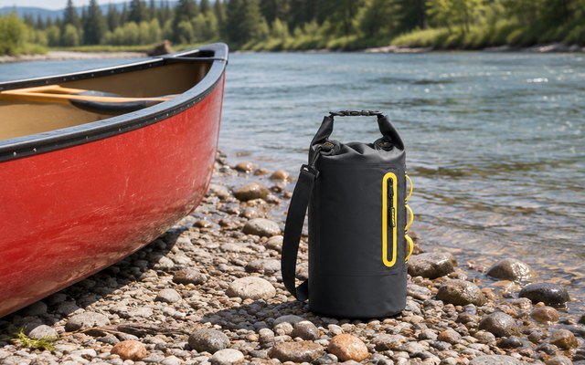 MARCHWAY floating dry bag, on a pebbly riverbank beside a red canoe pulled up on the shore