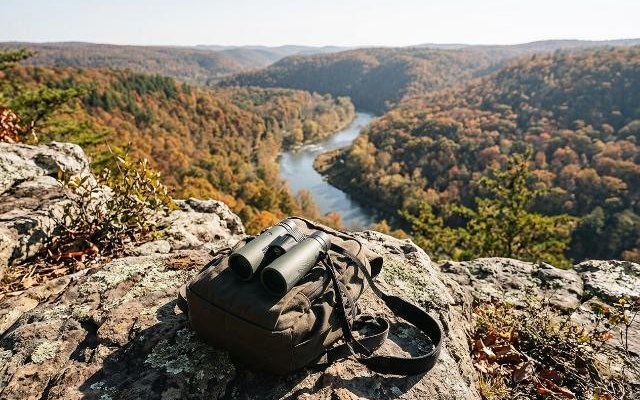 Green roof prism binoculars on a daypack at a rocky lookout over a river valley