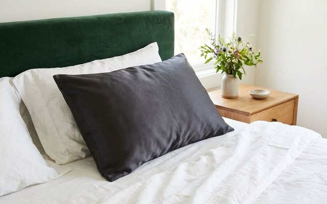 Pillow in a charcoal-grey silk pillowcase on a bed with a deep green velvet headboard