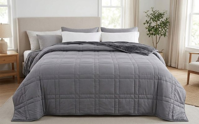 Large grey weighted blanket covering a king-size bed in a bright bedroom, top edge folded back