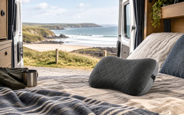 Camping pillow, on a bed in the back of a camper van parked by a British beach, the back doors open