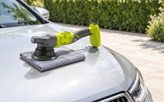 RYOBI 18V ONE+ cordless polisher resting on a microfibre cloth on the bonnet of a silver car on a sunny driveway