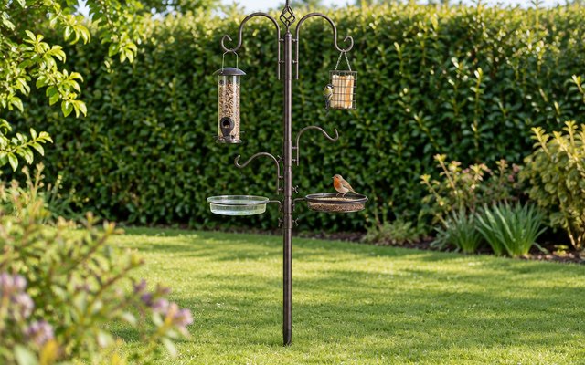 MIXXIDEA bird feeding station, standing in the middle of a lawn with a hedge behind