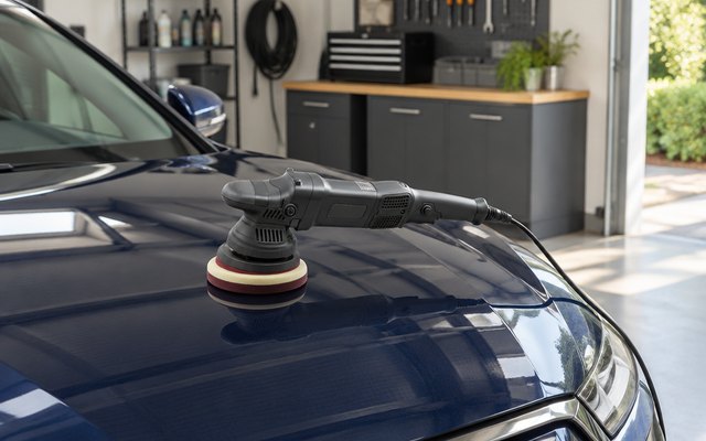 SPTA dual action polisher, resting on the hood of a dark blue car in a clean home garage