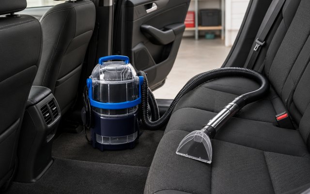 Portable spot cleaner by a car's open back seat in a garage