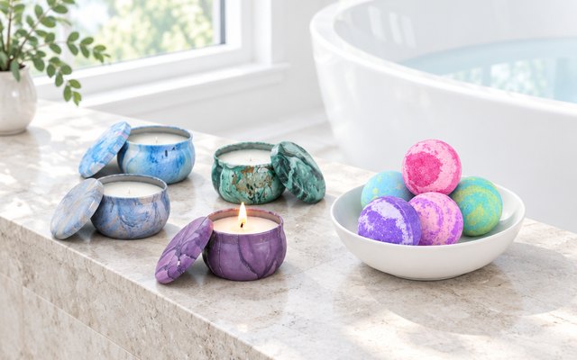 Marbled bath bombs in a bowl and tin candles on the ledge of a bright white bathtub