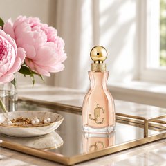 Jimmy Choo I Want Choo Eau de Parfum, perfume bottle on a mirrored vanity tray beside a few pink peonies and a small jewelry dish, soft window light