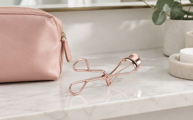 Eyelash curler, on a bathroom shelf beside a make-up bag