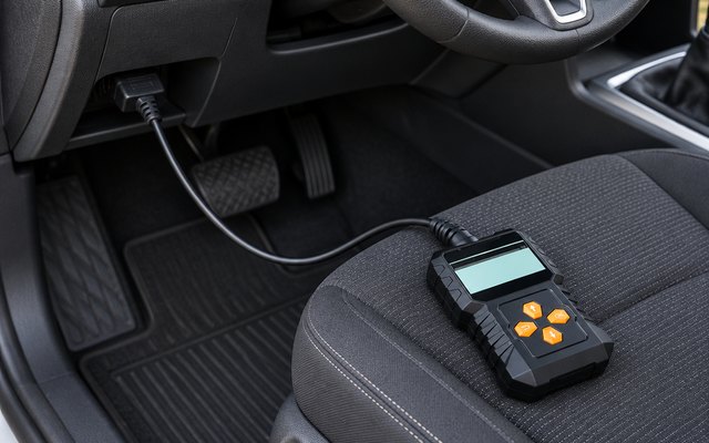 Small handheld OBD2 code reader lying on a car's driver seat