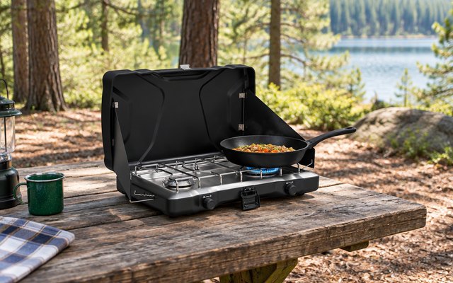 Coleman Triton 2-burner stove, on a picnic table at a forest campsite