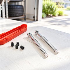 Two pencil tire gauges, a red case and spare valve caps on a white workbench in a bright garage