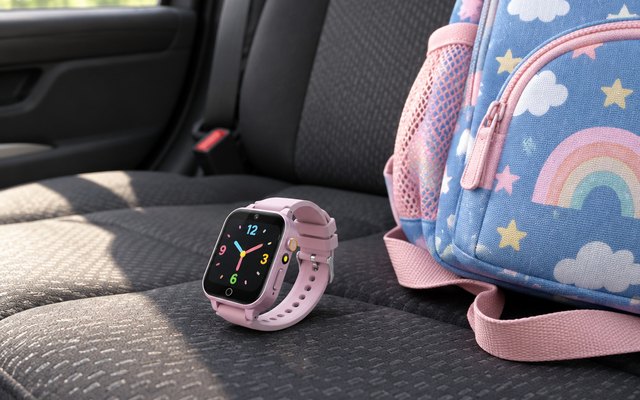 Kids' smartwatch, lying on the back seat of a car beside a kids' backpack, its screen showing a simple clock face