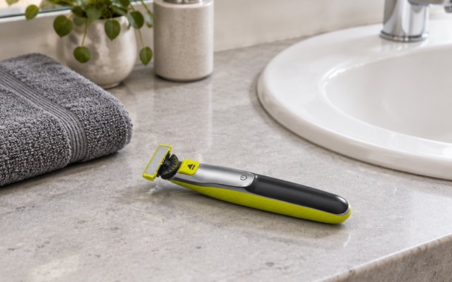 Lime and black hybrid trimmer lying on a bathroom counter beside the sink and a folded towel