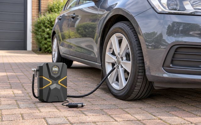 Portable tire inflator on a driveway, its hose screwed onto the front tire valve of a hatchback