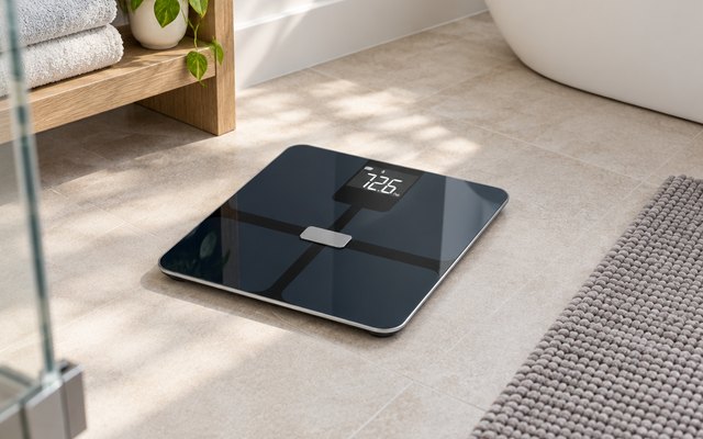 Glass smart scale on a bathroom floor beside a bath mat