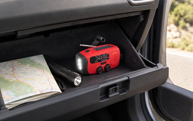 Emgykit pocket crank radio, in an open car glove box beside a road map and a flashlight