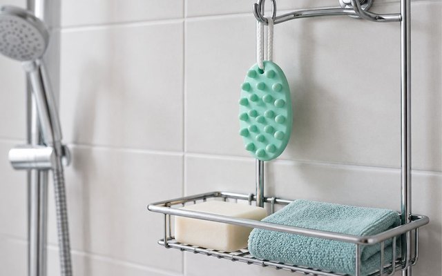 Green oval shampoo brush hanging from a shower caddy hook above a bar of soap