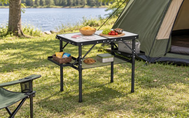 Titanker camping table, beside a tent in a grassy campground with a deck of playing cards and snacks on top