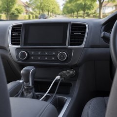 Belkin dual car charger, plugged into the dashboard socket of a family car, two cables running to the front seats, a leafy suburban street through the windscree
