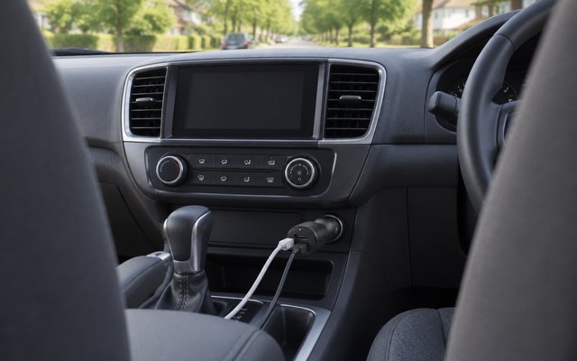 Belkin dual car charger, plugged into the dashboard socket of a family car, two cables running to the front seats, a leafy suburban street through the windscree