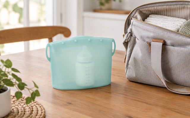 Dr. Brown's microwave steam sterilizer bag, on a wooden kitchen table beside an open diaper bag, ready for travel