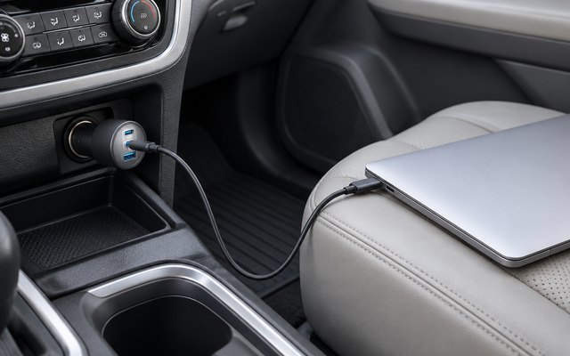 Anker Nano 167.5W car charger, plugged into the 12-volt socket of a minivan's front console, its cable leading to a plain silver laptop with no logo on the pass