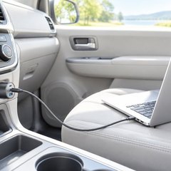 Car charger in a minivan’s console socket, its cable running to a laptop on the passenger seat