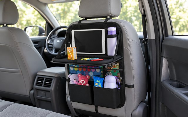 Oneyus backseat organizer with tray, strapped to the back of a front seat in a minivan, the tray folded down with a juice box and crayons on it