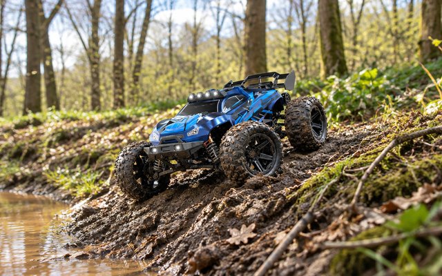 Womaqu RC truck, climbing a muddy bank at the edge of a woodland on a bright day