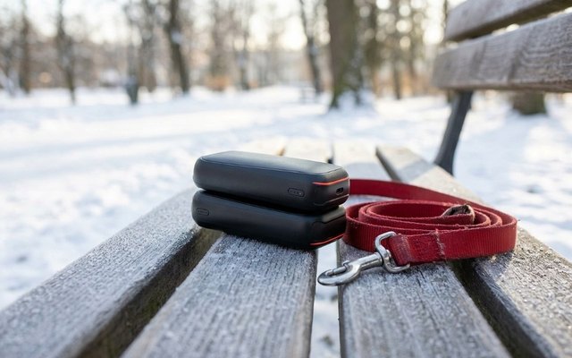 Black hand warmer pair with orange trim on a frosted park bench beside a red dog leash