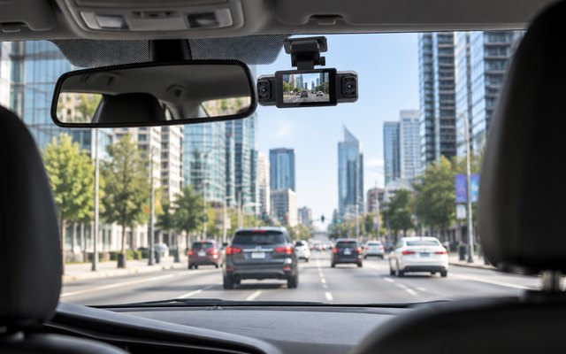 IIWEY N5 360-degree dash cam, mounted on the inside of a car's front window behind the rear-view mirror, seen from the back seat, a city street ahead in daylight