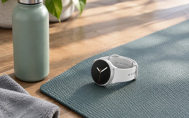 Silver round smartwatch lying on a yoga mat beside a water bottle