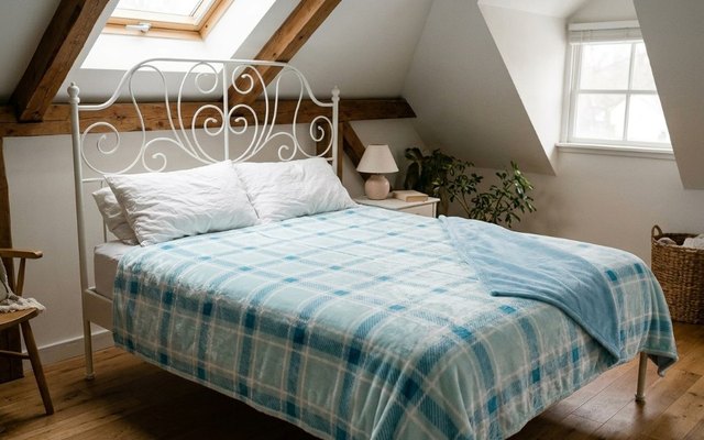 Light blue plaid heated blanket on a white iron bed in a bright attic bedroom