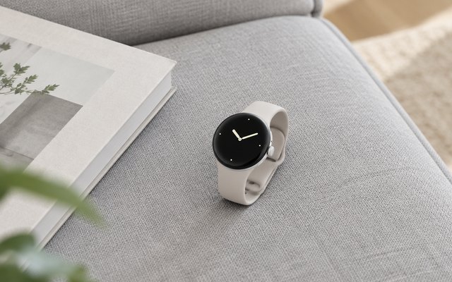 Round silver smartwatch with an off-white band on a grey sofa cushion