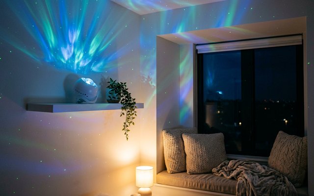 White round galaxy projector on a floating shelf in a reading nook, green and blue aurora light across the walls and ceiling