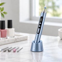 Cordless nail drill pen in its small charging stand on a manicure table beside bottles of nail polish and a few drill bits in a row