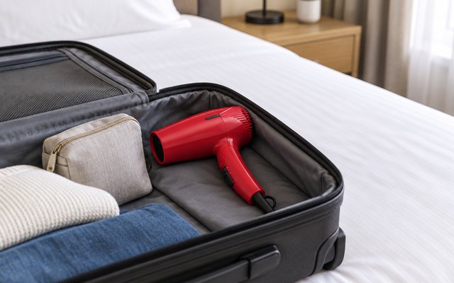 Folding travel hair dryer in an open suitcase on a hotel bed