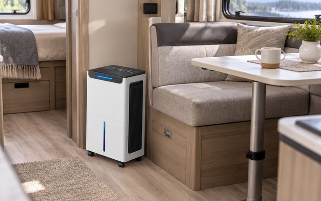 Compact compressor dehumidifier, on the floor of a clean modern RV interior beside the dinette