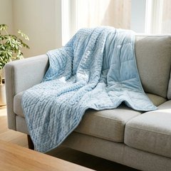 Light blue weighted blanket with raised dots draped over a grey sofa in a sunny living room