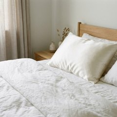 Pillow in a natural white silk pillowcase on a bed made with white linen